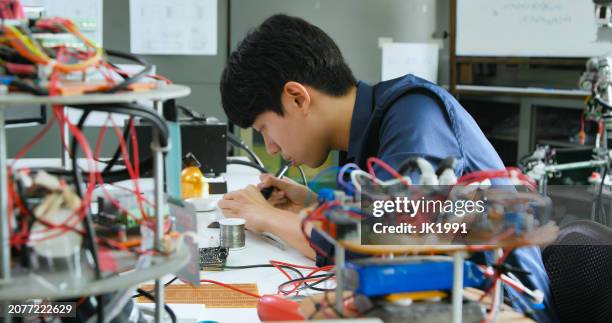 asian male technician soldering electronic parts in lab. - prototype stock pictures, royalty-free photos & images