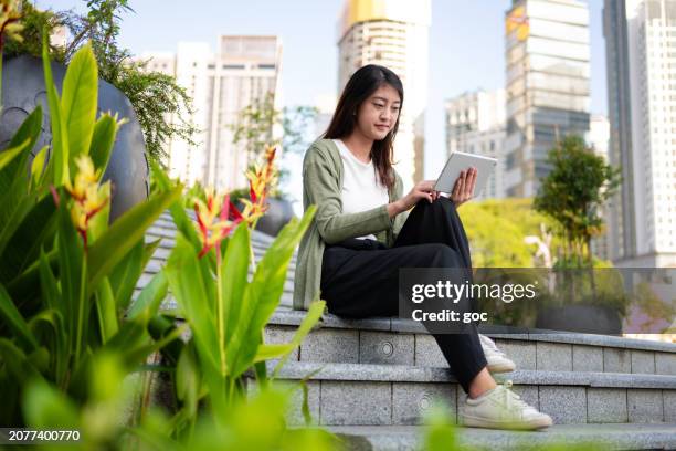 joven mujer de negocios asiática usando tableta digital mientras está sentada en las escaleras - vista a nivel del ojo fotografías e imágenes de stock