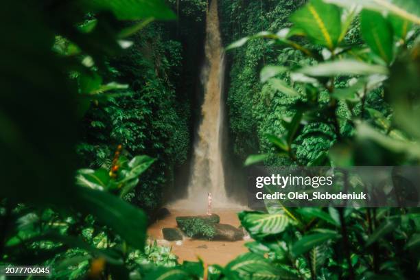 woman standing near the powerful waterfall on bali - rainy season stock pictures, royalty-free photos & images