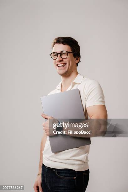 portrait of a young adult man holding a laptop - looking away stock pictures, royalty-free photos & images