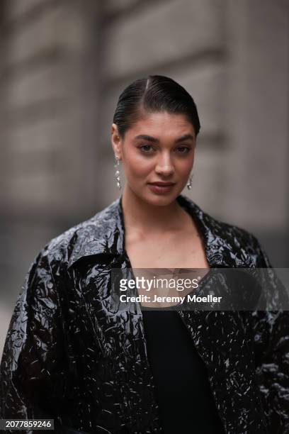 Sarah Posch seen wearing Pilgrim silver earrings, H&M black cotton jumpsuit and Boss black shiny varnished leather oversized long coat, on March 09,...