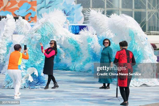 People pose for photos with 'sea wave' art installation made of tens of thousands of environmentally-friendly straws at a shopping center on March...