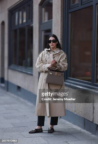 Tugba Kement seen wearing YSL black sunglasses, COS beige oversized long coat, black long suit pants, Hermès Kelly taupe / brown leather bag, gold...