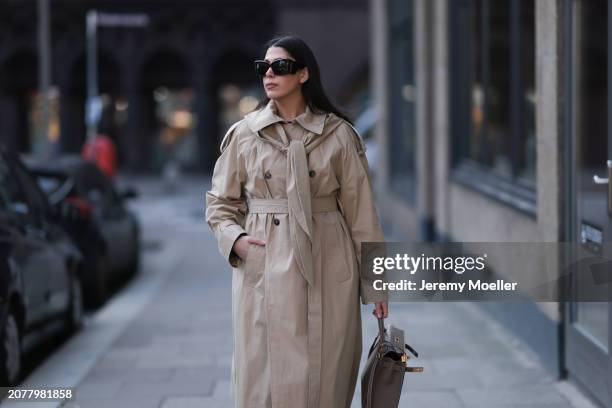 Tugba Kement seen wearing YSL black sunglasses, COS beige oversized long coat, Hermès Kelly taupe / brown leather bag and gold rings, on March 08,...