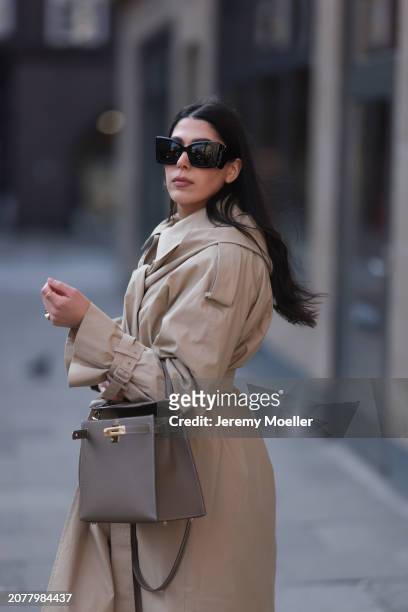 Tugba Kement seen wearing YSL black sunglasses, COS beige oversized long coat, Hermès Kelly taupe / brown leather bag and gold rings, on March 08,...