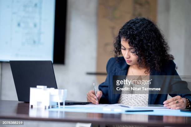 cost contol in building design and construction to ensure financial stability in your construction project. a female construction project manager working on construction breakdown cost and budget review in a design office space. - bim stock pictures, royalty-free photos & images
