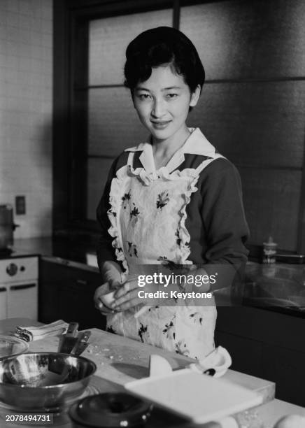 Crown Princess Michiko of Japan wearing an apron while cooking in the kitchen of Togu Palace in Tokyo, October 1961.