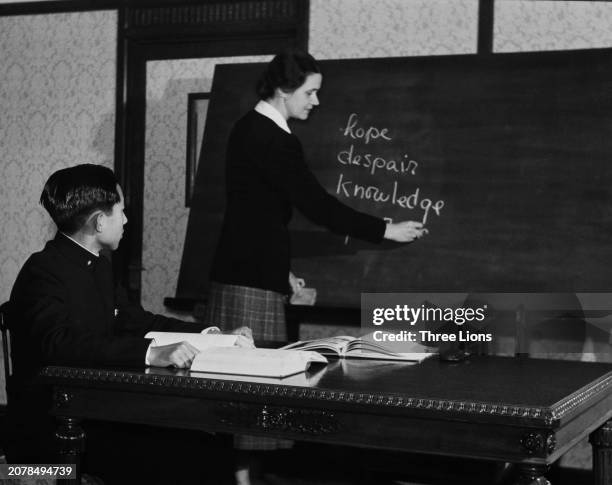 Crown Prince Akihito, wearing the uniform of Peers' School, watches his American tutor, Elizabeth Gray Vining , as she writes the words 'hope,...