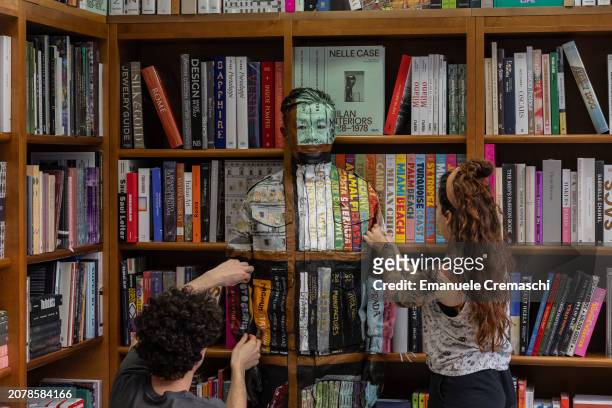 Two assistants paint some details of the camouflage of Chinese artist Liu Bolin as he prepares to perform at Libreria Hoepli on March 12, 2024 in...