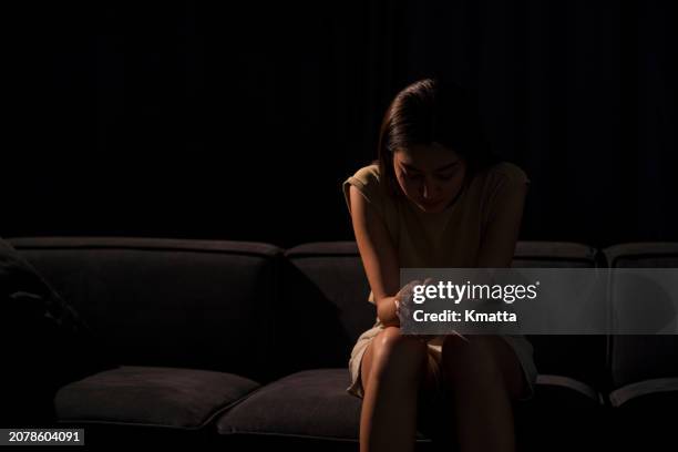 depressed young woman sitting lonely on sofa in darkness. - pouca luz imagens e fotografias de stock