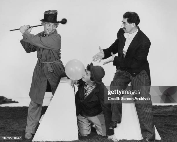 Harpo Marx, swings golf club at Chico Marx as Groucho Marx looks on in comic pose for their 1939 Marx Brothers comedy 'At the Circus' .