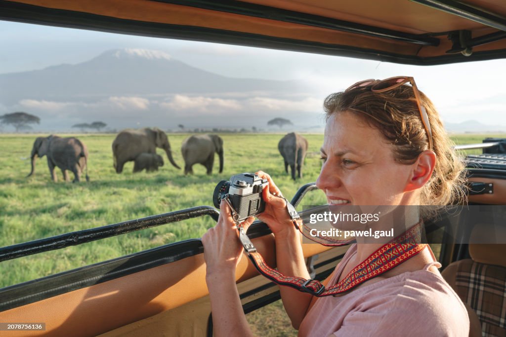Woman enjoying safari with elephants and Kilimanjaro mountain during sunset Amboseli National Park, Kenya