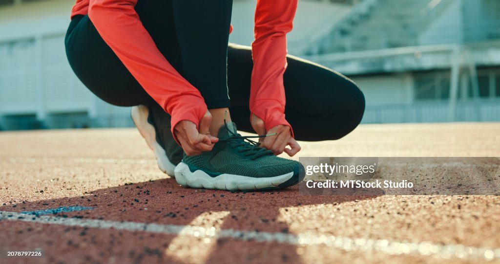 Closeup of young Asian female athlete runner tying shoelaces in preparation for running exercise getting ready for jogging outdoors. Healthy workout exercise.