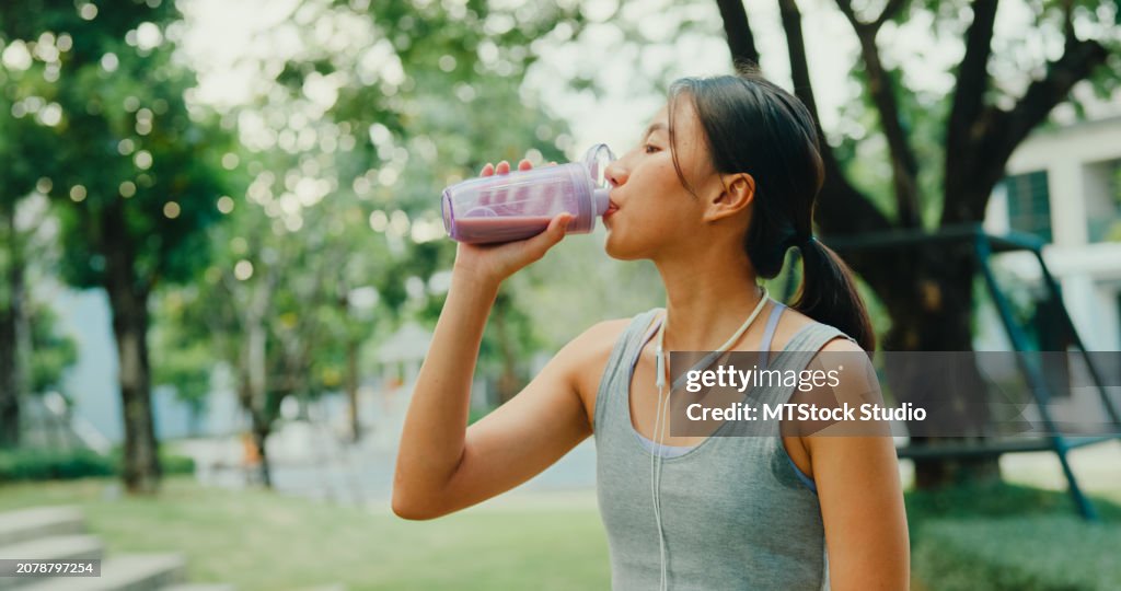 Young Asian female athlete runner drinking protein shake after exercise workout in urban park. Diet and healthy food workout exercise.