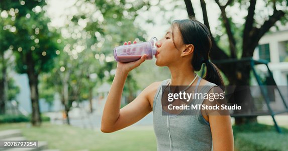 Young Asian female athlete runner drinking protein shake after exercise workout in urban park. Diet and healthy food workout exercise. Young Asian female athlete runner drinking protein shake after exercise workout in urban park. Diet and healthy food workout exercise.