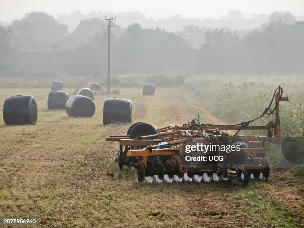 Electricity pylon, farm machinery and bale silage bags in Radley Village at dawn.