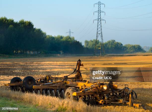 Electricity pylon and farm machinery in a Radley field at dawn.