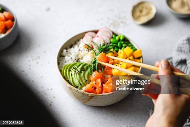 nahaufnahme einer frau, die frische und leckere poke bowl mit essstäbchen isst - asiatische küche stock-fotos und bilder