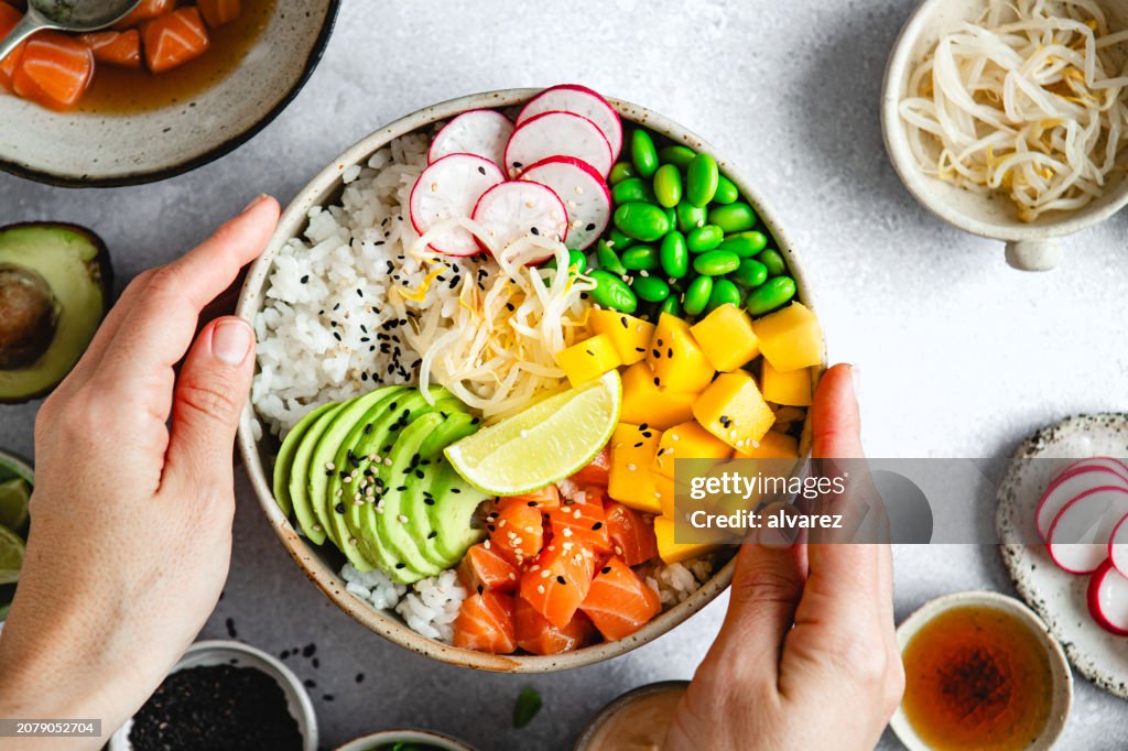 Top view of woman hands holding a poke bowl with salmon on kitchen table