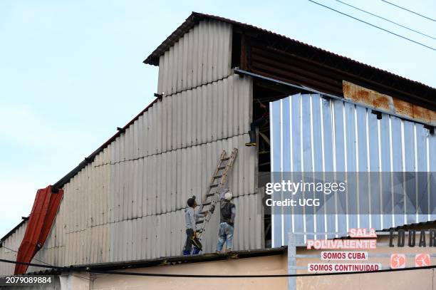 Santa Clara, Cuba, Two men repairing the metallic walls of the Sala Polivalente . There is a sign reading Somos Cuba, Somos Continuidad.