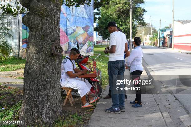 Santa Clara, Cuba, A man works self-employed re-filling gas lighters. Other Cuban people stands in the sidewalk waiting for his service.