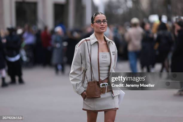 Guest seen wearing Miu Miu hair clips, Miu Miu brown round glasses, Miu Miu beige jacket with brown leather details, Miu Miu strapless top, matching...