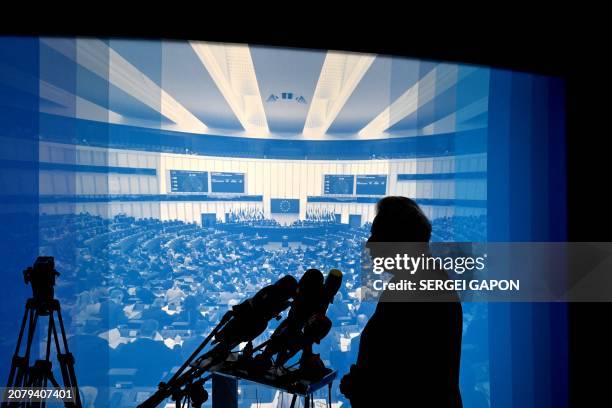 European Commissioner for Agriculture Janusz Wojciechowski is silhouetted against a backdrop showing a European Parliament pleanary as he presents...