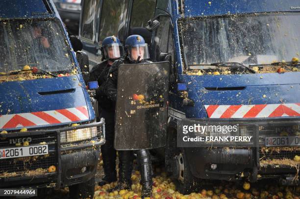 French gendarms stand next to vans covered with crushed apples, on October 16 in the French western city of Nantes, during a protest gathering...