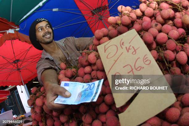 Un vendeur de litchis rend la monnaie en euro devant une pile de fruits dont le prix comporte encore le double affichage, franc et euro, le 31...