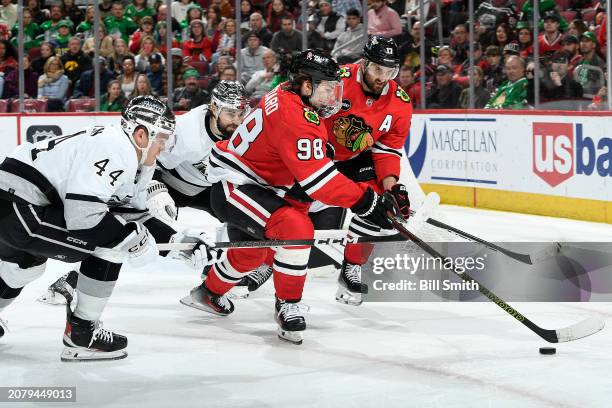 Connor Bedard of the Chicago Blackhawks carries the puck through Mikey Anderson of the Los Angeles Kings and Drew Doughty of the Los Angeles Kings...
