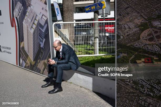 Businessman looks at his telephone sitting on a low wall at the Mipim in Cannes. The MIPIM Fair in Cannes, southern France, is considered to one of...