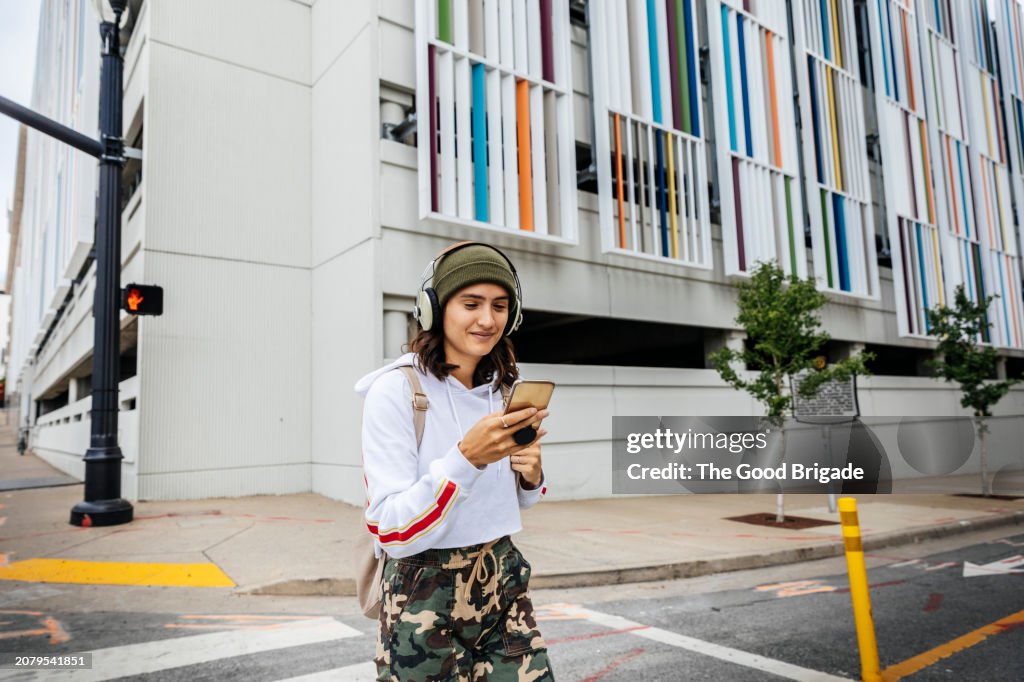 Smiling woman using smart phone while crossing street in city
