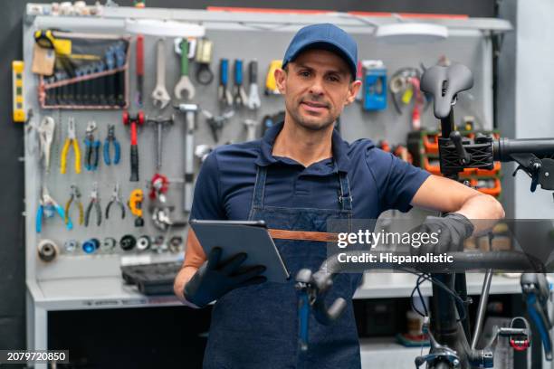 mechanic fixing a bicycle at the repair shop and using a digital tablet - hispanolistic stockfoto's en -beelden