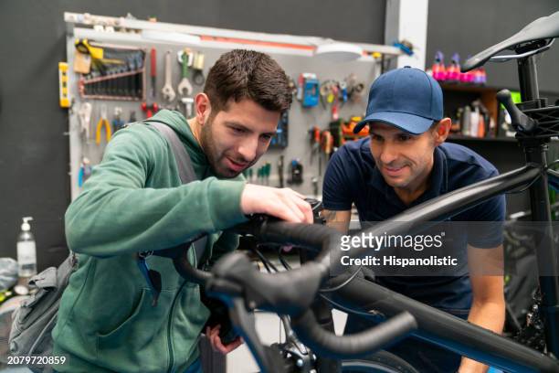 mecánico hablando con un hombre sobre su bicicleta en un taller de reparación - hispanolistic fotografías e imágenes de stock