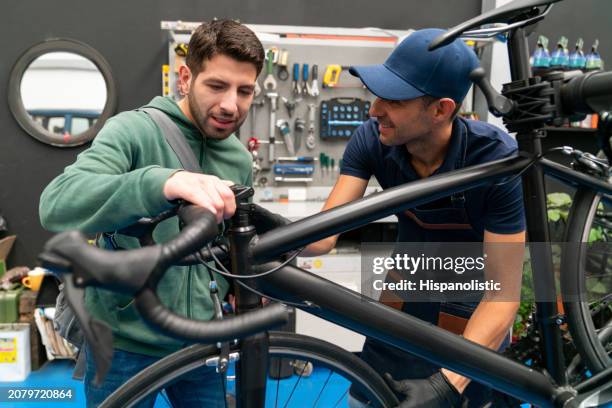 hombre hablando de su bicicleta con el mecánico de un taller de reparación - hispanolistic fotografías e imágenes de stock