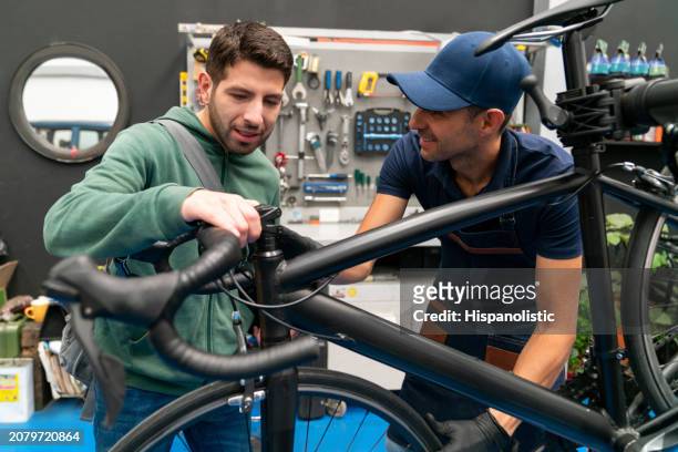 man talking about his bicycle to the mechanic at a repair shop - hispanolistic stockfoto's en -beelden