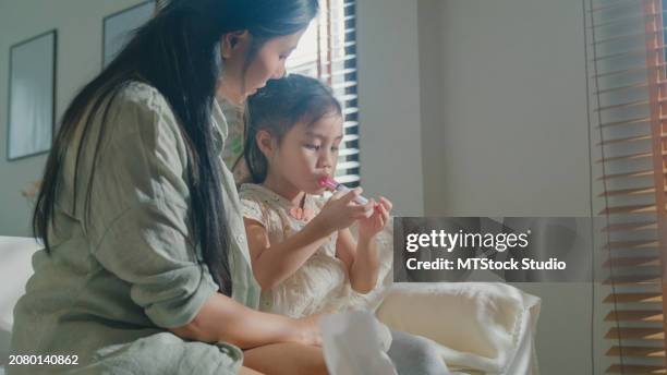 mom takes care of her daughter who gets sick and has a high fever and feeds liquid medicine to her child via syringe at home. illness girl with a medical condition and family wellness. - hand over mouth stock pictures, royalty-free photos & images