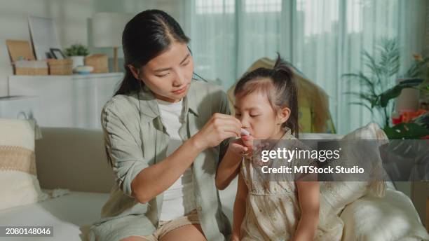 mom takes care of her daughter who gets sick and has a high fever, cold, and flu, and feeds medicine to her child at home. illness girl with a medical condition and family wellness. - throat stock pictures, royalty-free photos & images