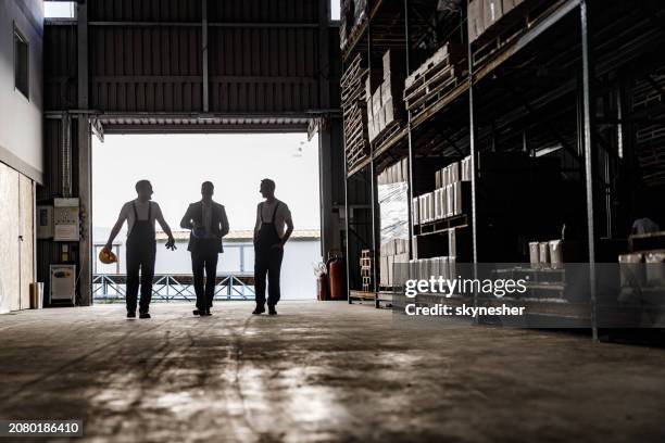 happy workers and their manager talking on the move in storage room. - dark warehouse stock pictures, royalty-free photos & images