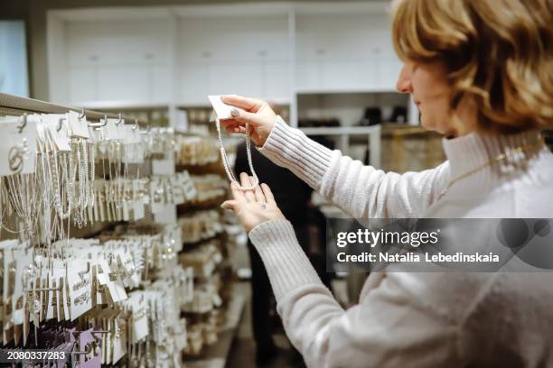 accessory selection: woman in a sweater browses jewelry in a clothing store, focusing on accessorizing her outfit - accessorizing stockfoto's en -beelden