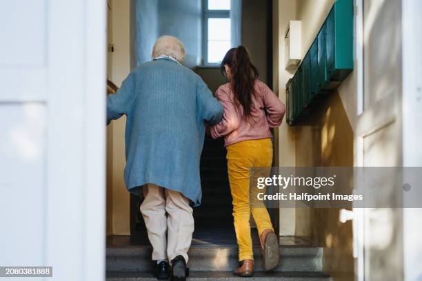 granddaughter helping senior grandmother walk up the stairs, going grocery shopping. girl holding hand of her elderly woman, providing stability while walking. - world kindness day stock pictures, royalty-free photos & images