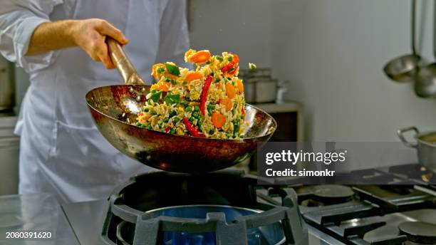 chef tossing a fried rice dish in a wok - wok stockfoto's en -beelden