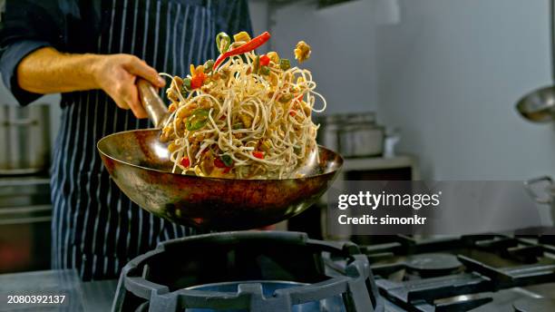 chef holding a wok and tossing a noodle stir fry dish - wok stock pictures, royalty-free photos & images