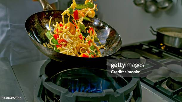 noodles with prawns and vegetable falling into a heated wok and being tossed by the chef - frigideira chinesa imagens e fotografias de stock