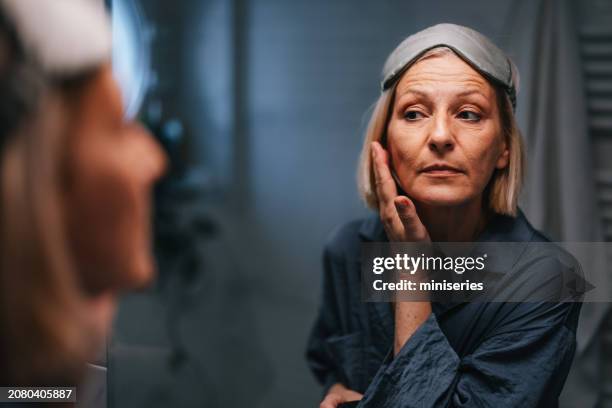primer plano de una mujer mayor mirándose en el espejo y revisando su cara y arrugas - arrugado fotografías e imágenes de stock
