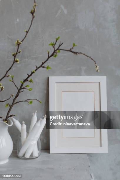 blank picture frame next to cherry plum branches in a jug and candles on a mantelpiece - photo frame on mantle piece stockfoto's en -beelden