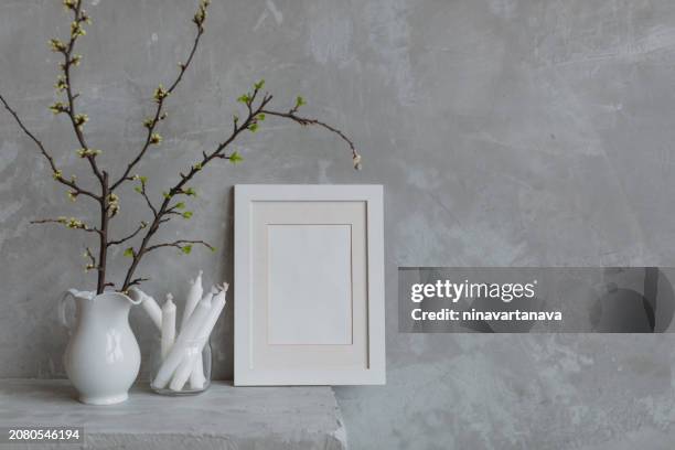 blank picture frame next to cherry plum branches in a jug and candles on a mantelpiece - photo frame on mantle piece stockfoto's en -beelden