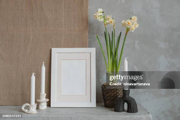 blank picture frame next to a flowering narcissus plant and candles on a table - photo frame on mantle piece stockfoto's en -beelden