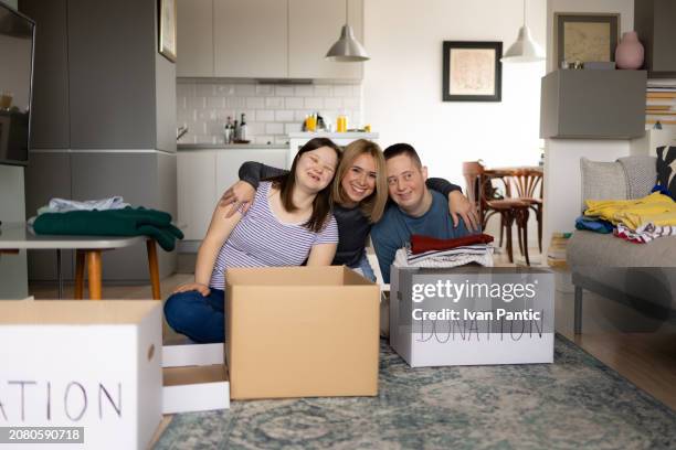 happy donation manager embracing her friends with special needs at home. - man holding donation box stock pictures, royalty-free photos & images