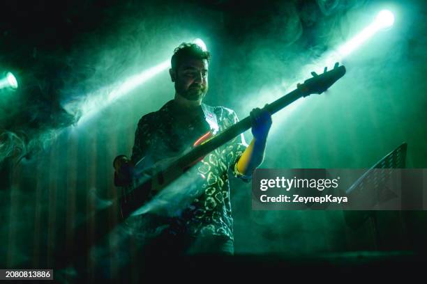 bassgitarrist der music band auf der bühne mit rauch- und lichteffekten - boygroup stock-fotos und bilder